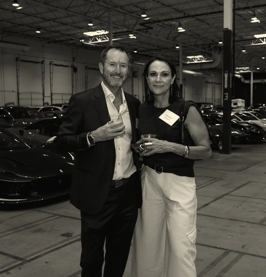 Two guests sharing a drink beside a supercar